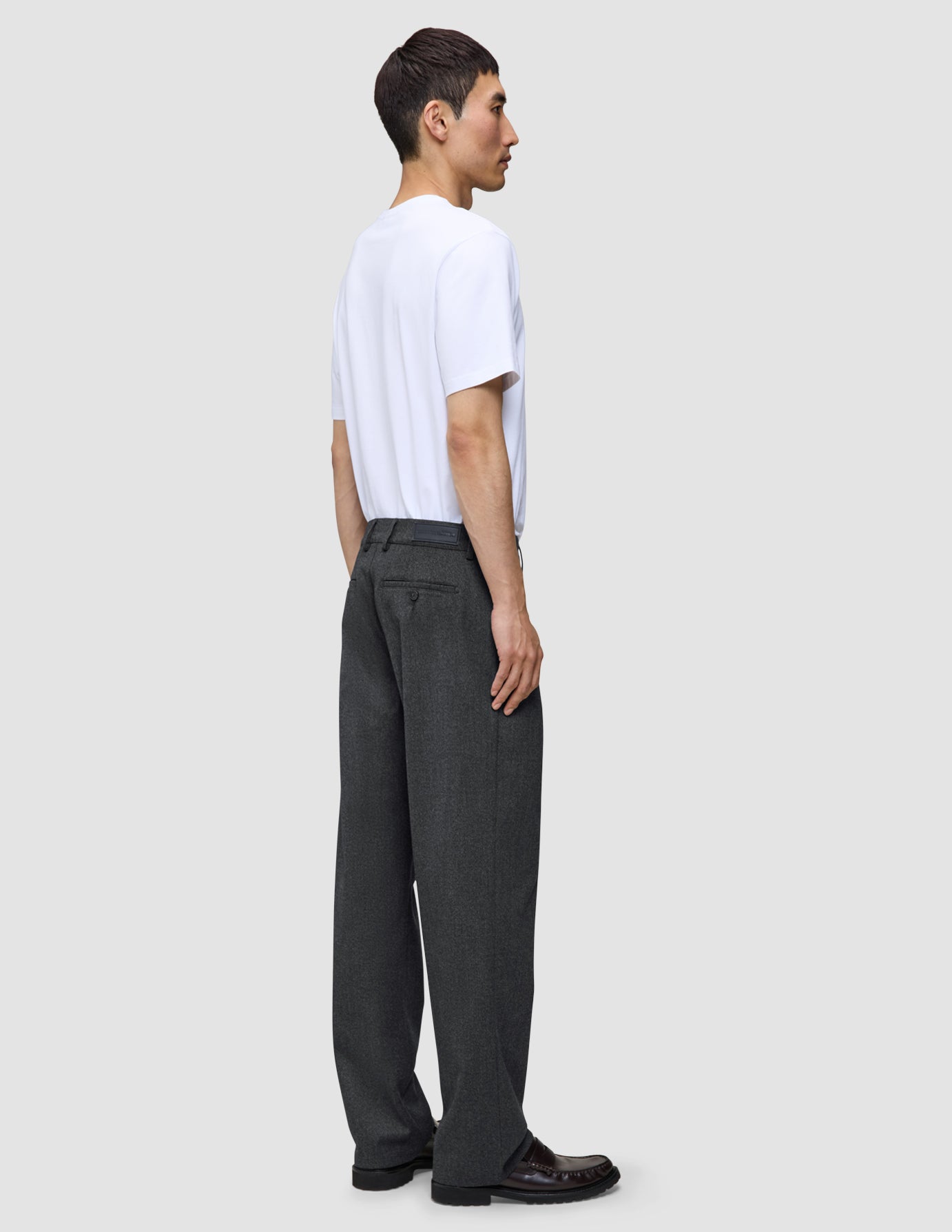 En mann sett i profil har på seg en hvit T-skjorte og Atelier Pants Relaxed Dark Grey i mørkegrå, løstsittende brutt twill.